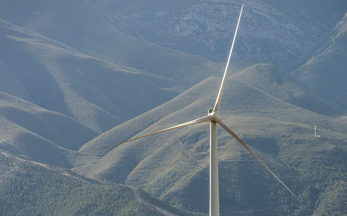 A wind turbine standing on a hillside above a valley